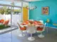 Palm Springs style dining table with Saarinen tulip chairs and table and orange and yellow dishware and stemware